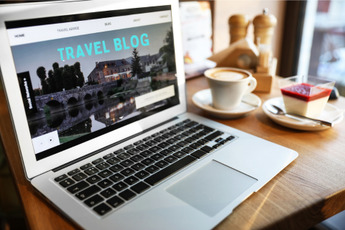a laptop with a webpage of a travel blog on the screen. there is a coffee and dessert on the table next it 