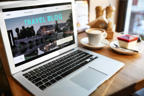 a laptop with a webpage of a travel blog on the screen. there is a coffee and dessert on the table next it 